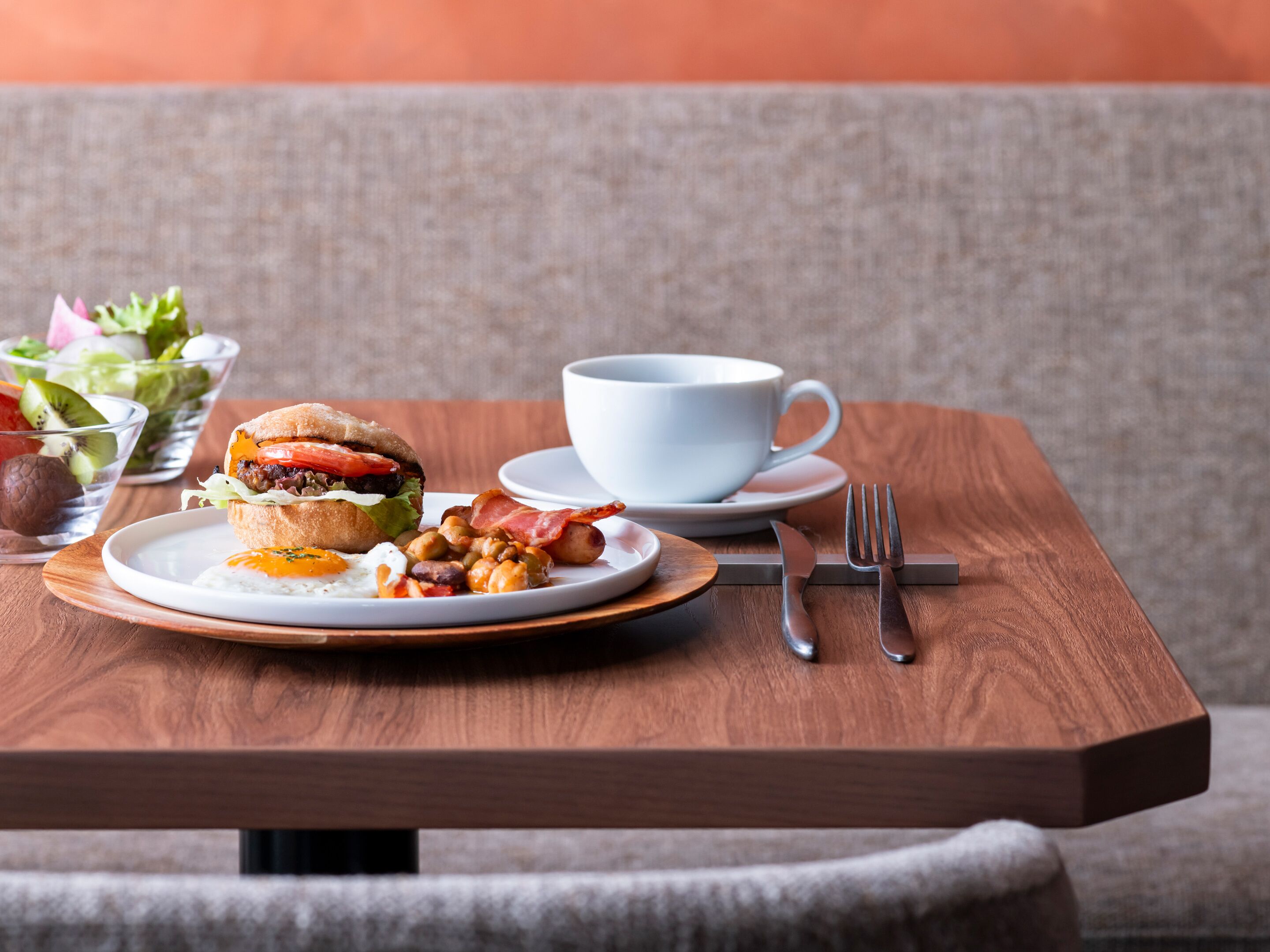 A breakfast setting with a plate of food, a cup, and cutlery on a wooden table.