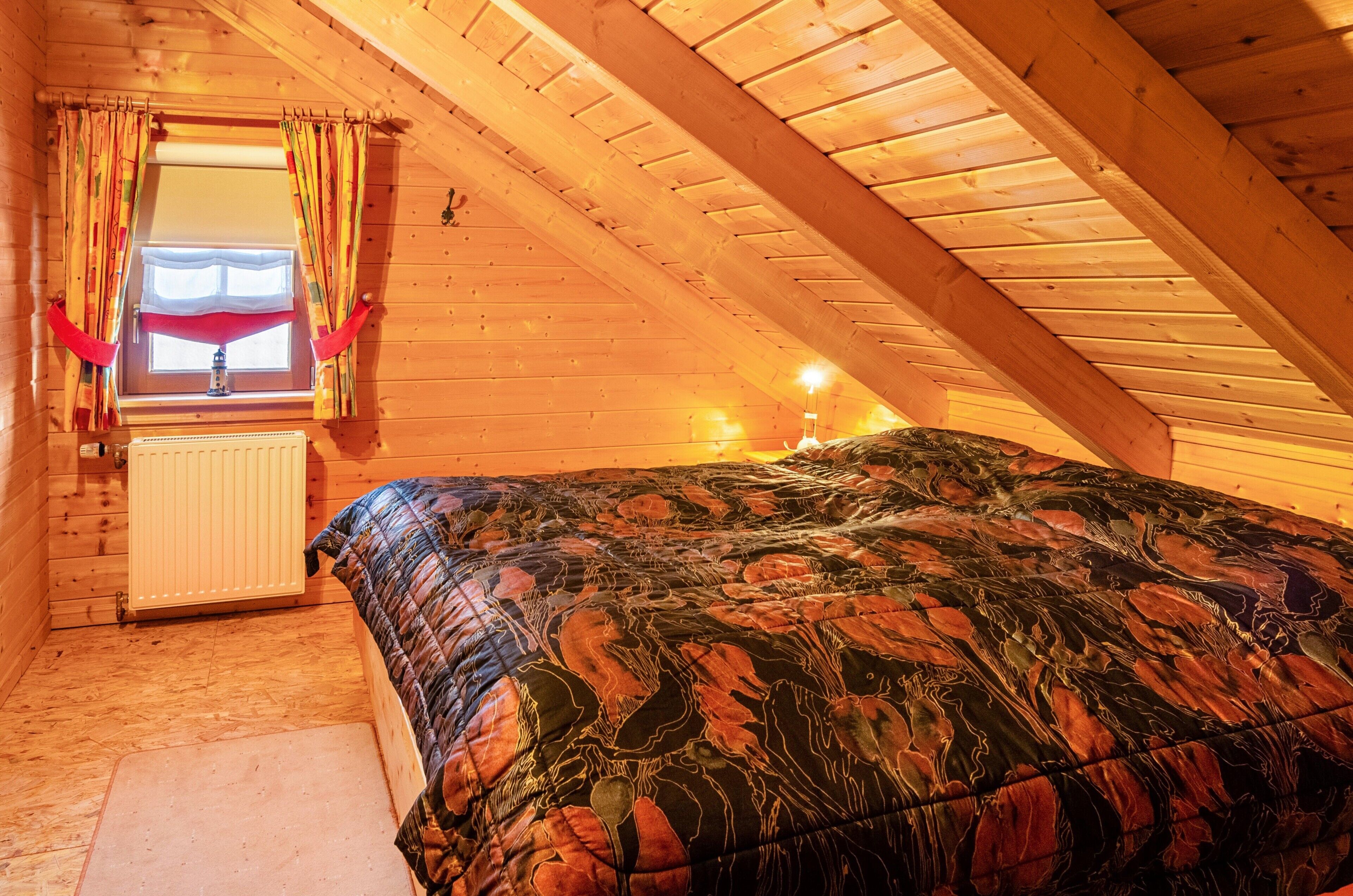 A wooden attic bedroom with a bed, a radiator, and a window with curtains.