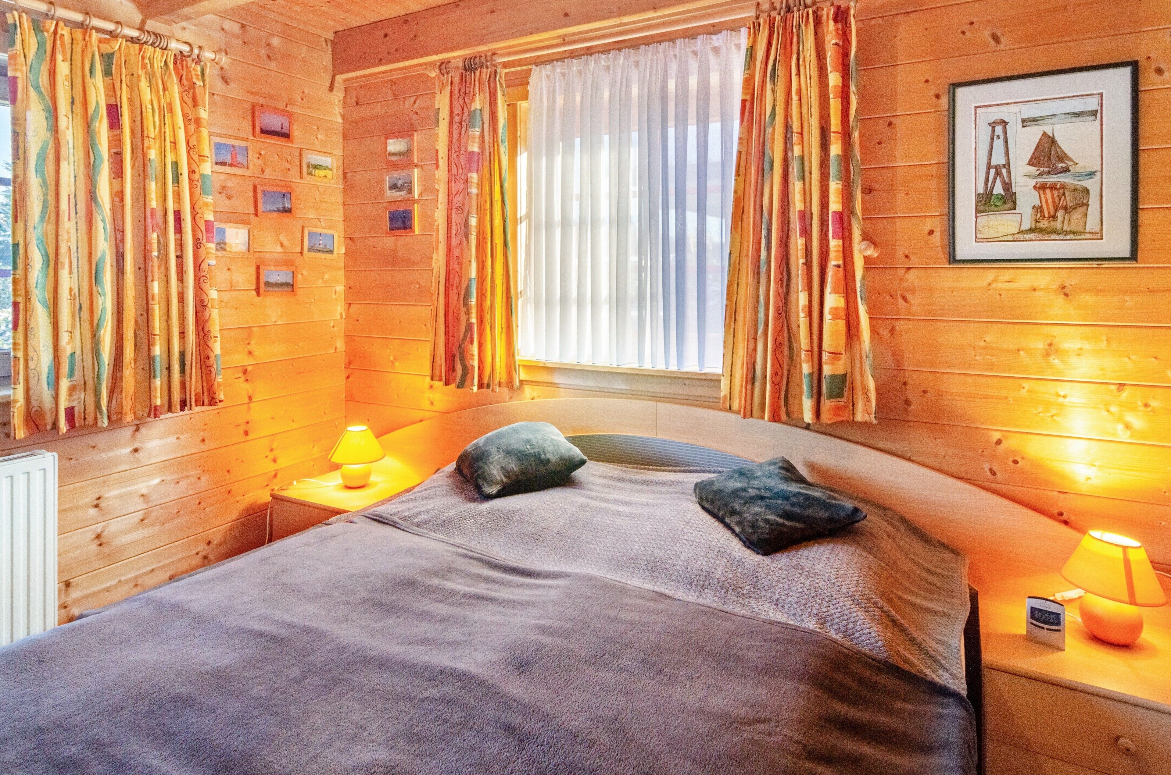 Un dormitorio de cabaña de madera con una cama, almohadas, una mesita de noche con una lámpara, una ventana con cortinas y un cuadro en la pared.