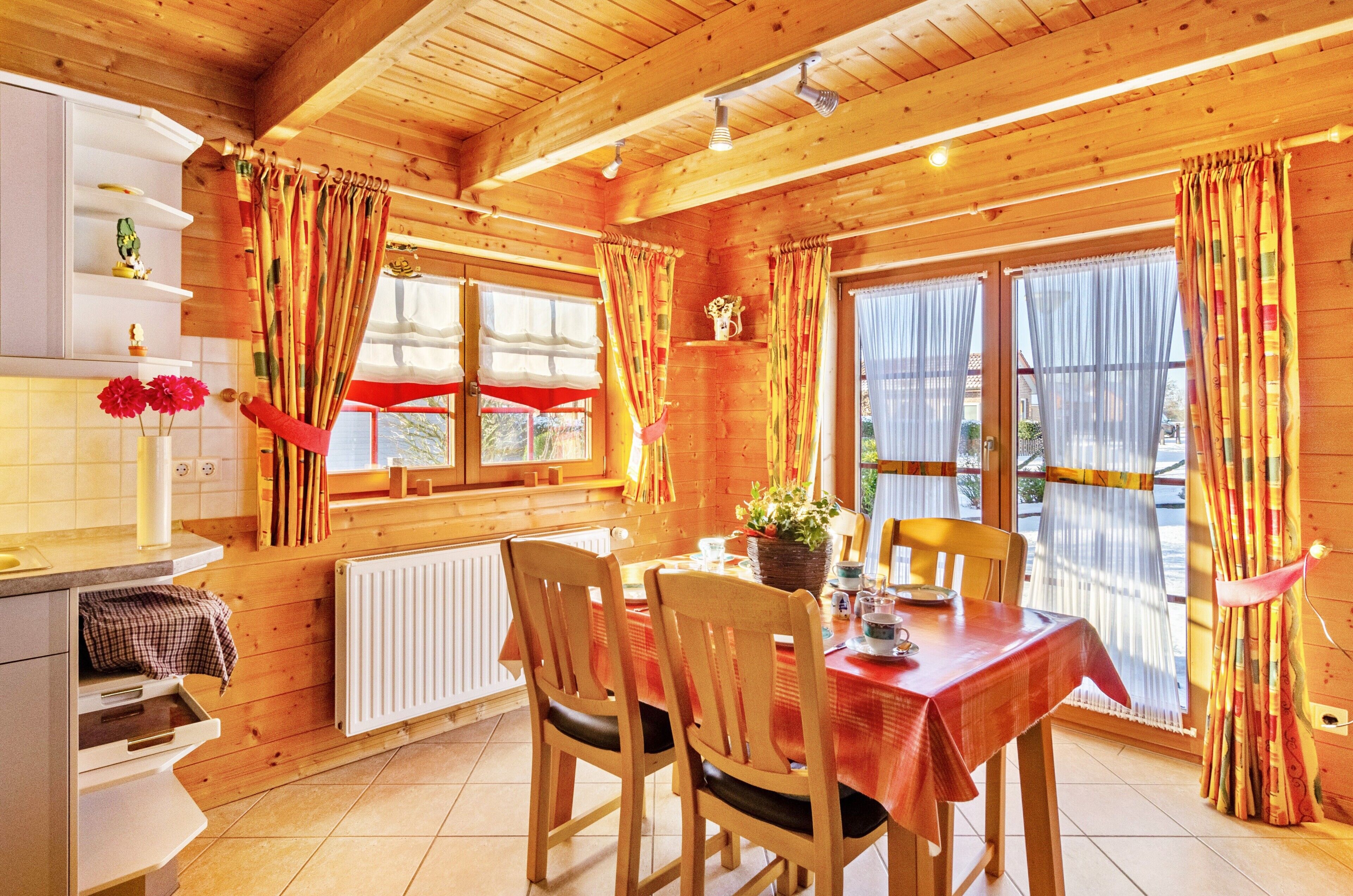 A wooden interior with a dining table, chairs, and a kitchen area with a radiator.