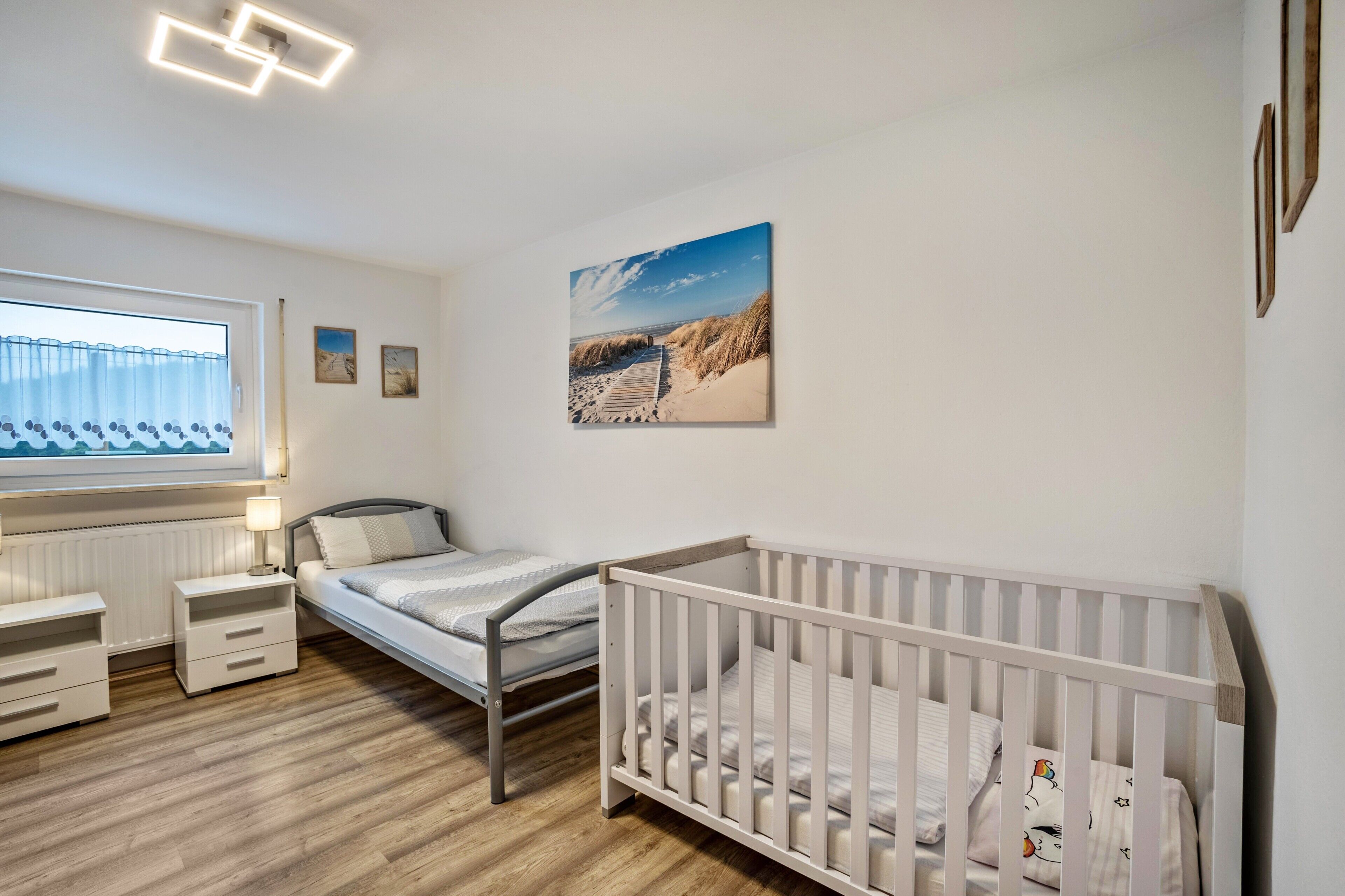 Une chambre de bébé avec un berceau, un lit, une table de chevet, une lampe et une fenêtre donnant sur la plage.