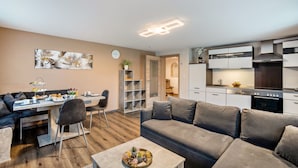 A modern living space with a dining area, a sofa, a coffee table, and a kitchen with white cabinets and a stove.