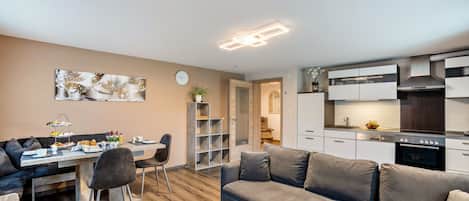 Un espacio habitable moderno con comedor, sofá, mesa de centro y cocina con armarios blancos y estufa.