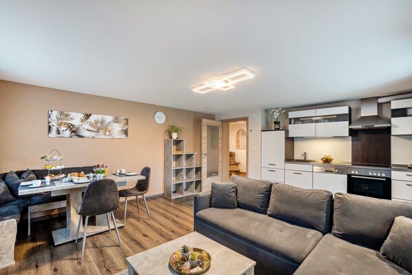 Un espace de vie moderne comprenant un coin repas, un canapé, une table basse et une cuisine avec des meubles blancs et une cuisinière.