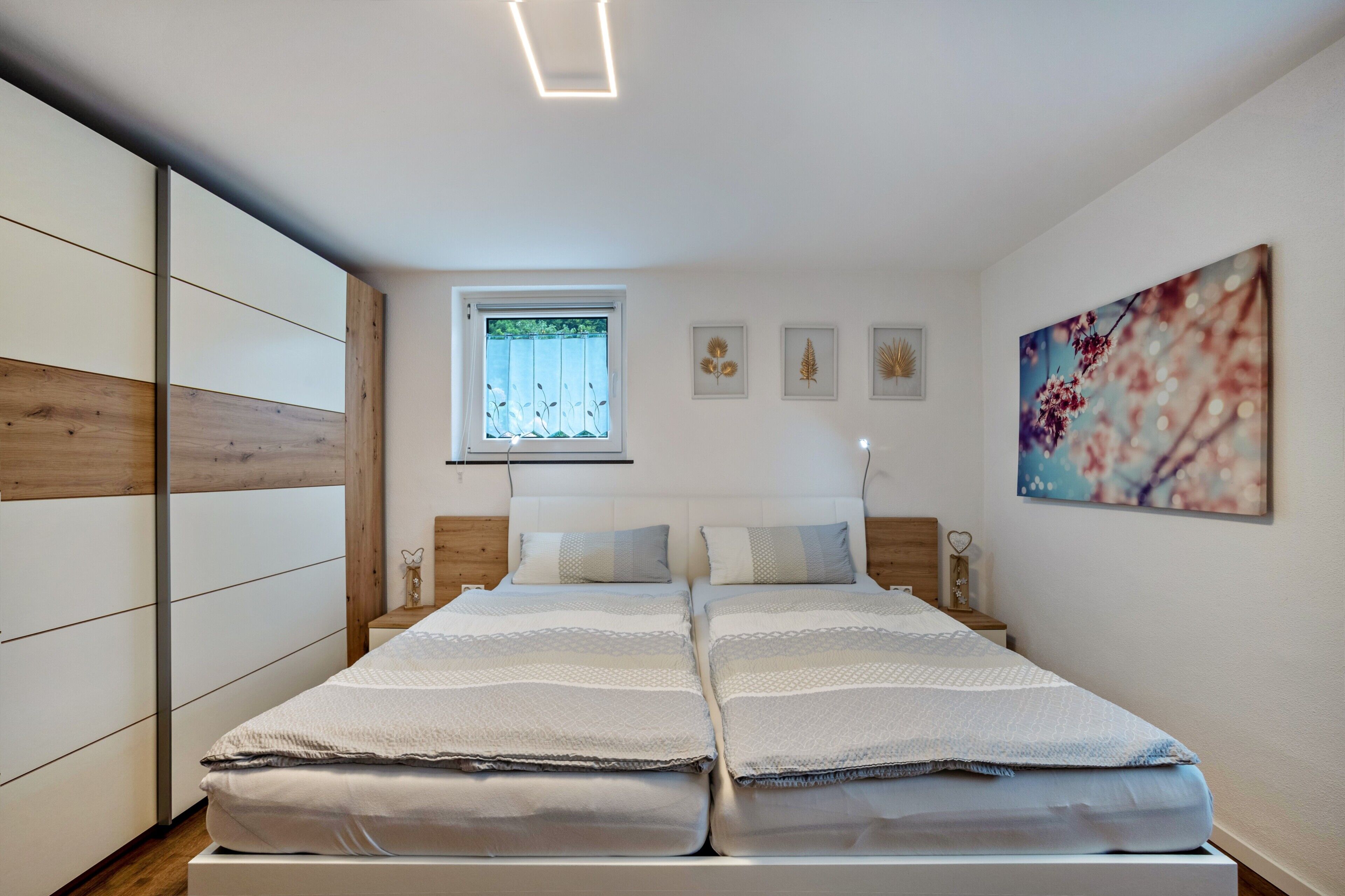 A double bed with a headboard, a window with blinds, and a wall-mounted artwork.