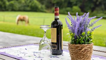 A bottle of wine, a wine glass, and a lavender plant on a table with a floral tablecloth.