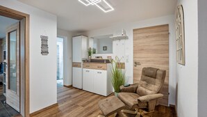 A modern interior with a wooden floor, a brown leather chair, a small ottoman, a kitchen area with white cabinets, and a mirror.