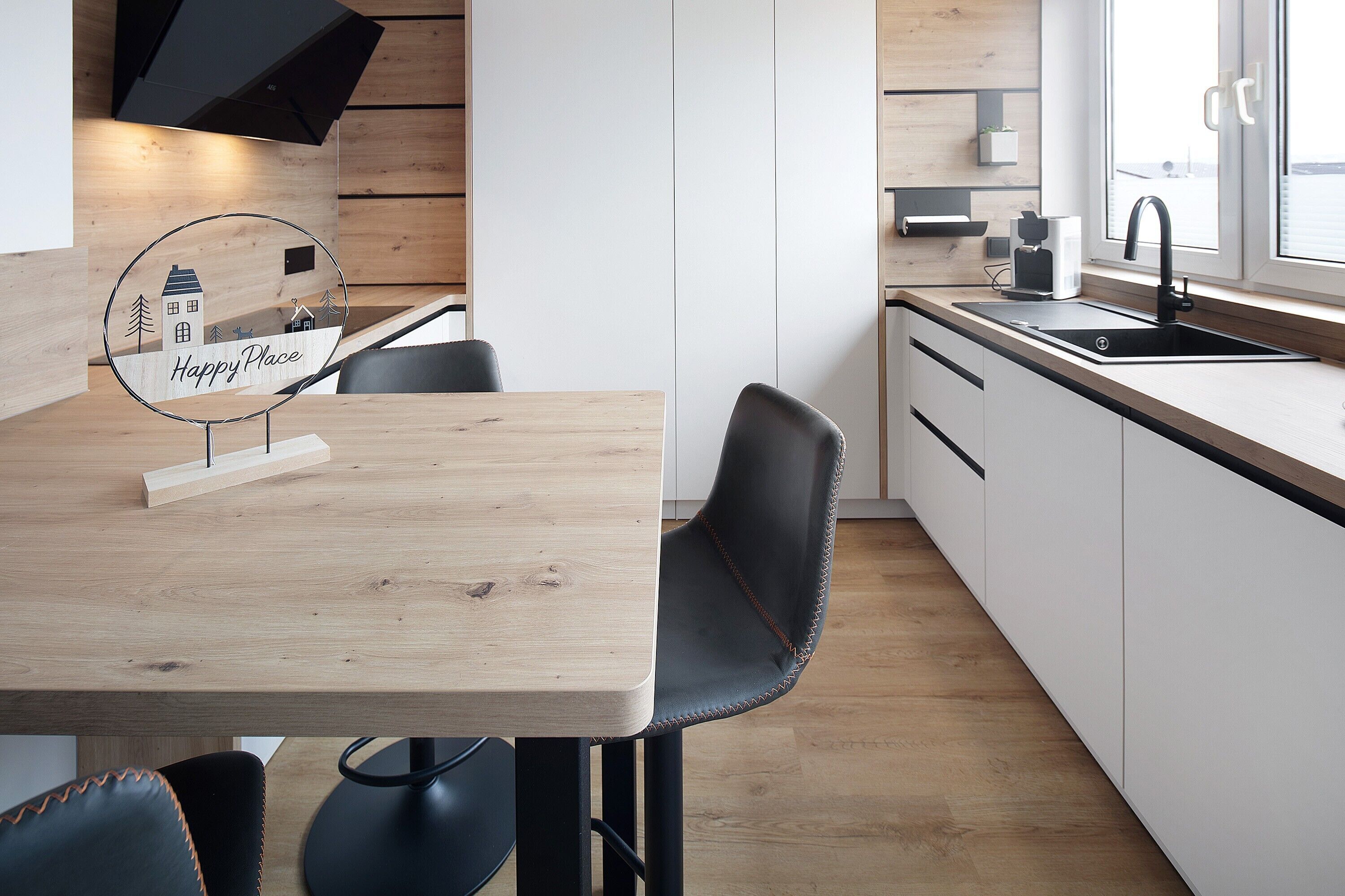 A modern kitchen with a wooden table, black chairs, a black faucet, and a window with a view.