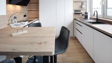 A modern kitchen with a wooden table, black chairs, a black faucet, and a window with a view.