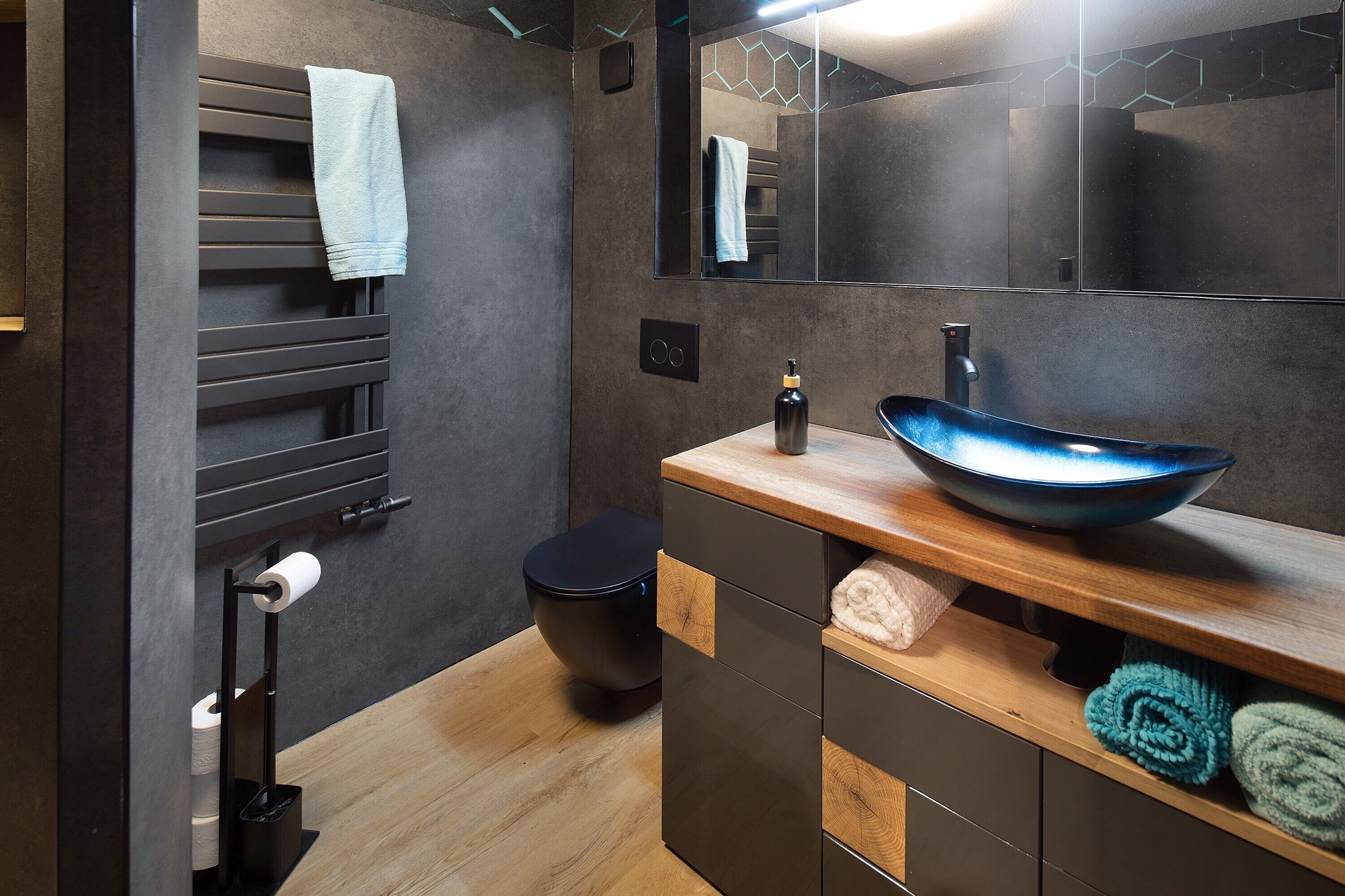Ein modernes Badezimmer mit einer schwarzen Toilette, einem hölzernen Waschtisch mit einer blauen Waschbecken und einem Handtuchhalter mit einem weißen Handtuch.