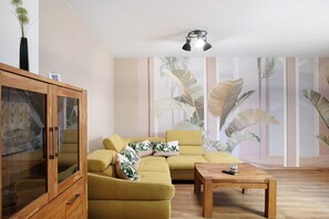 Una sala de estar con un sofá seccional, una mesa de centro de madera, un aparador con puertas de vidrio y un candelabro en el techo.