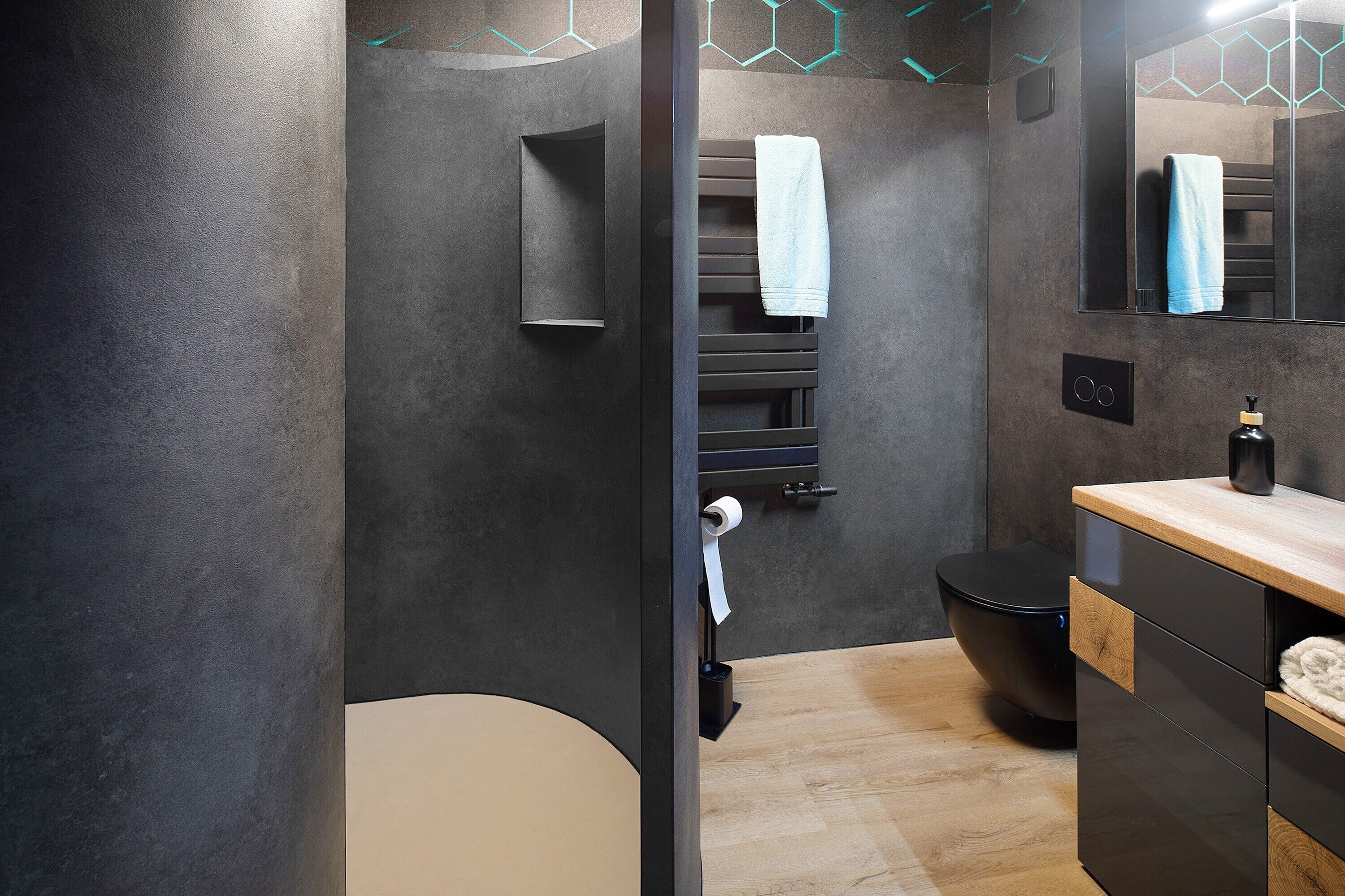 Ein modernes Badezimmer mit dunkler Wand, einem hölzernen Waschtisch, einer Toilette und einem Handtuchhalter.