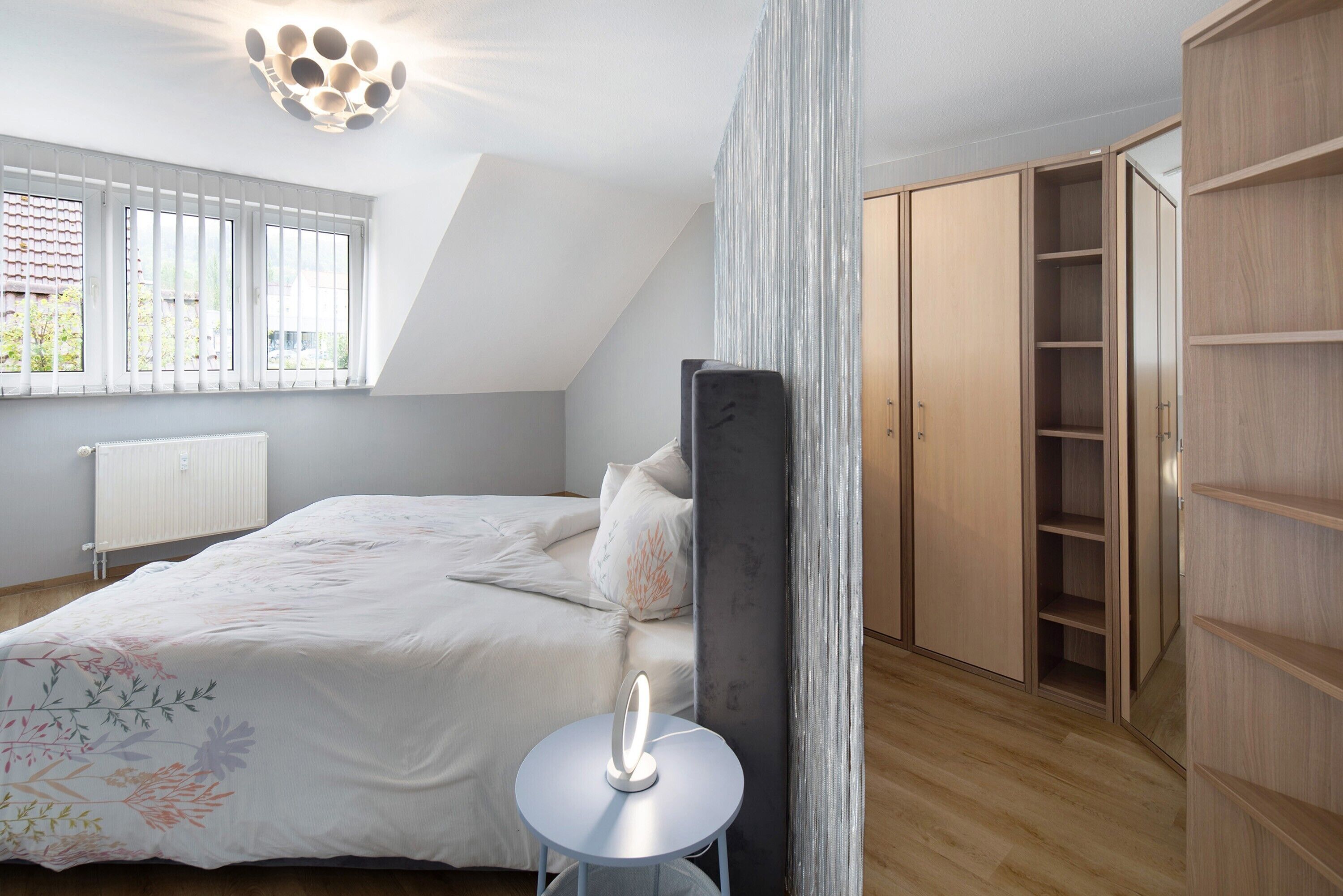 Une chambre à coucher comprenant un lit, une table de chevet, une armoire et une fenêtre avec des stores.