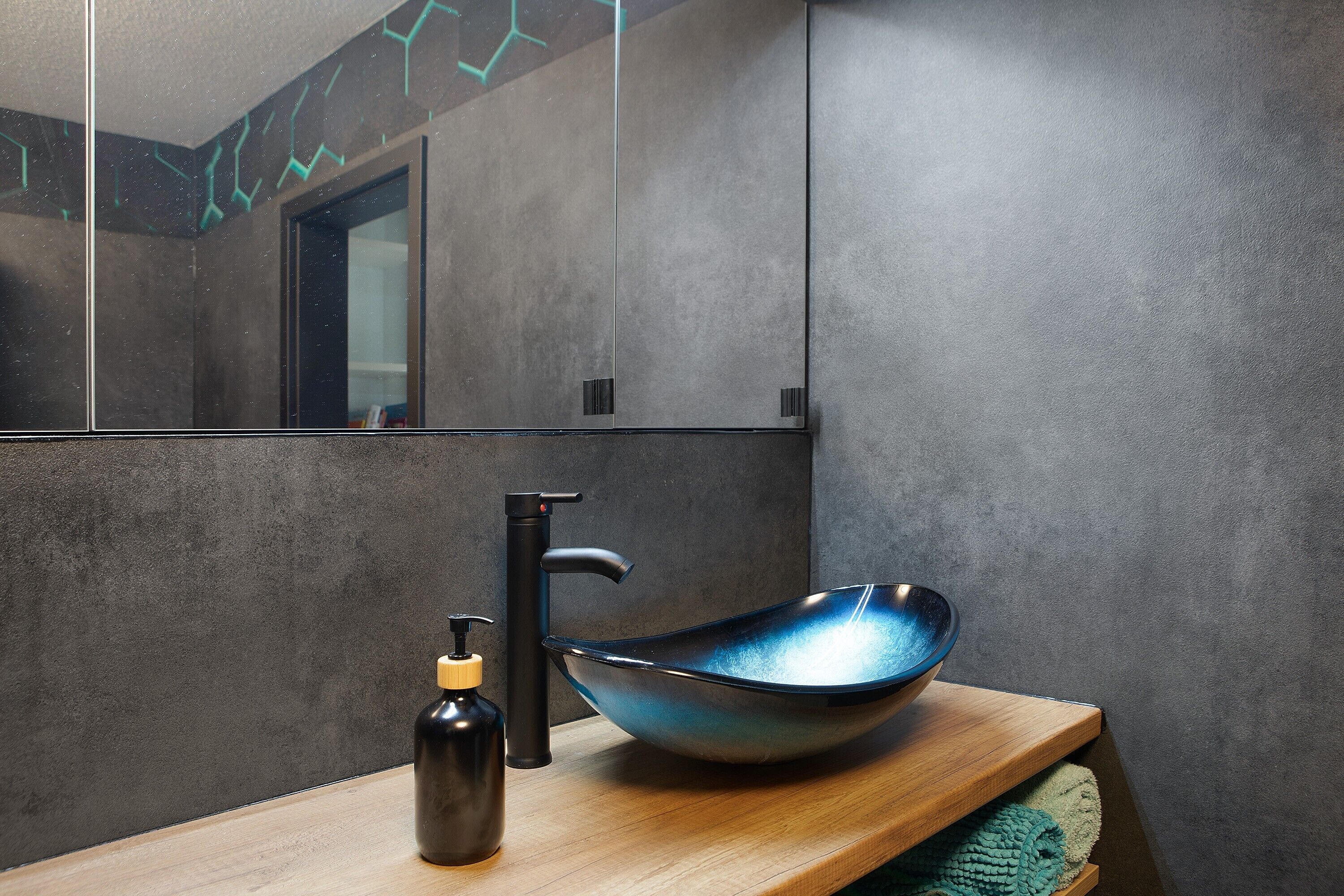 A bathroom with a modern sink, a mirror, and a wooden shelf.