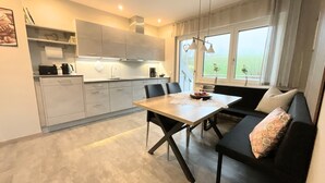 A modern kitchen with a dining area, a sofa, and a view of the outdoors. - Apartment 'Wiesenblick' with Balcony and Wi-Fi (Brilon)