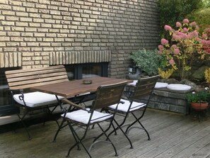 A wooden deck with a brick wall, a wooden table, and chairs. - Apartment 'Wiesenblick' with Balcony and Wi-Fi (Brilon)