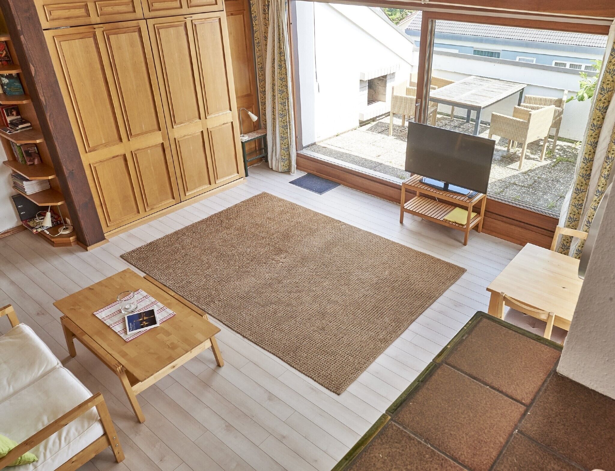 Un salon avec un téléviseur, des meubles en bois, un grand tapis et une vue sur l’extérieur.