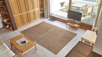 Un salon avec un téléviseur, des meubles en bois, un grand tapis et une vue sur l’extérieur.
