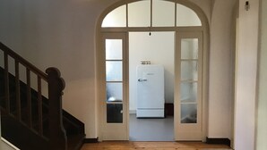 Un pasillo con escalera de madera, un refrigerador blanco y una pequeña mesa.