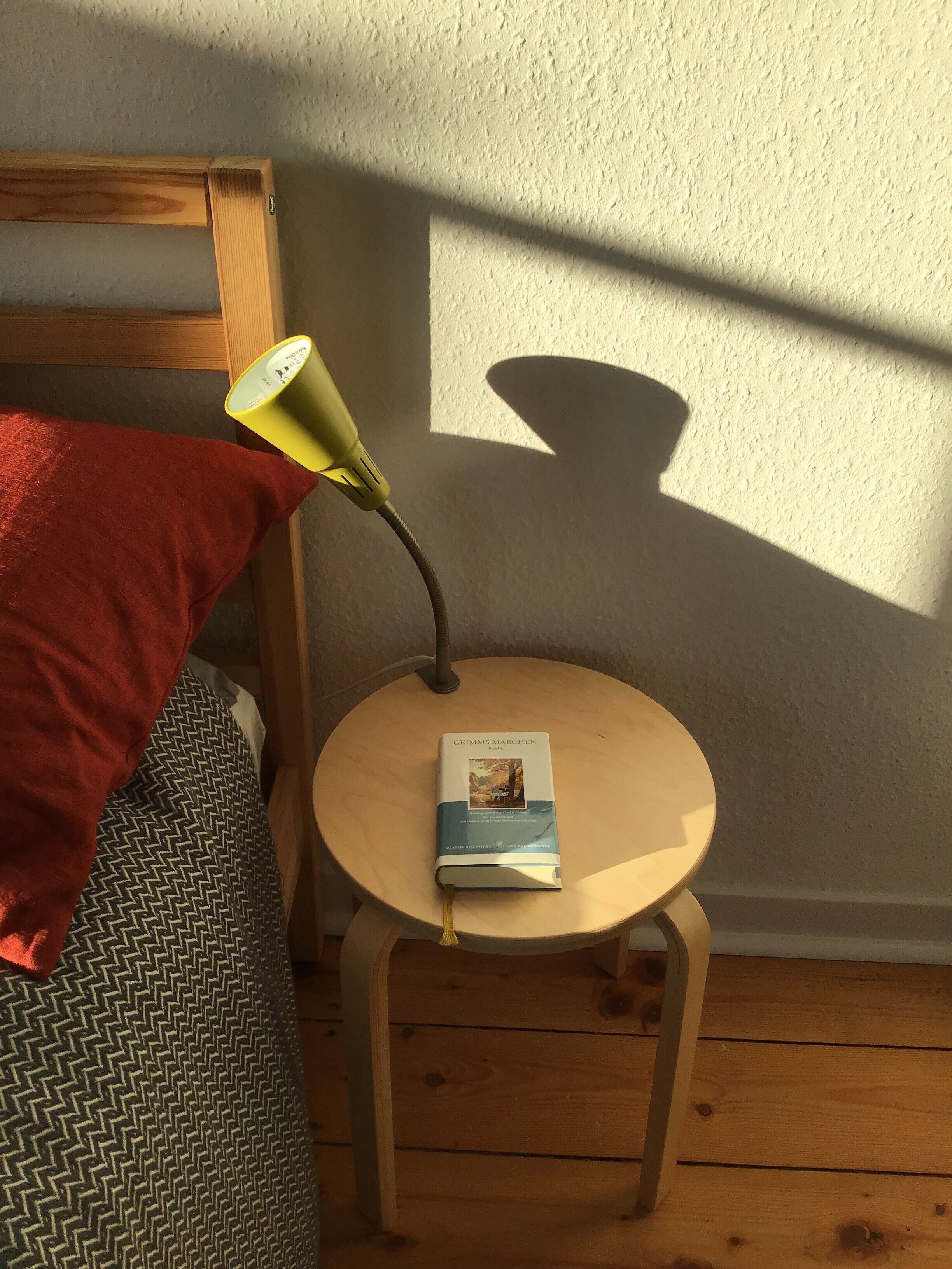 Ein kleiner, runder Holztisch mit einem Buch mit dem Titel 'Grimms Marchen', einer Lampe und einem roten Kissen auf einer Couch.