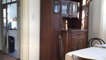 Un comedor con una mesa y sillas de madera, un mueble bajo de madera oscura con puertas de cristal, y un acceso a otra habitación.