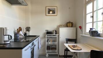 A compact kitchen with a stove, oven, and a small table with a cutting board.