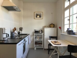A compact kitchen with a stove, oven, and a small table with a cutting board.