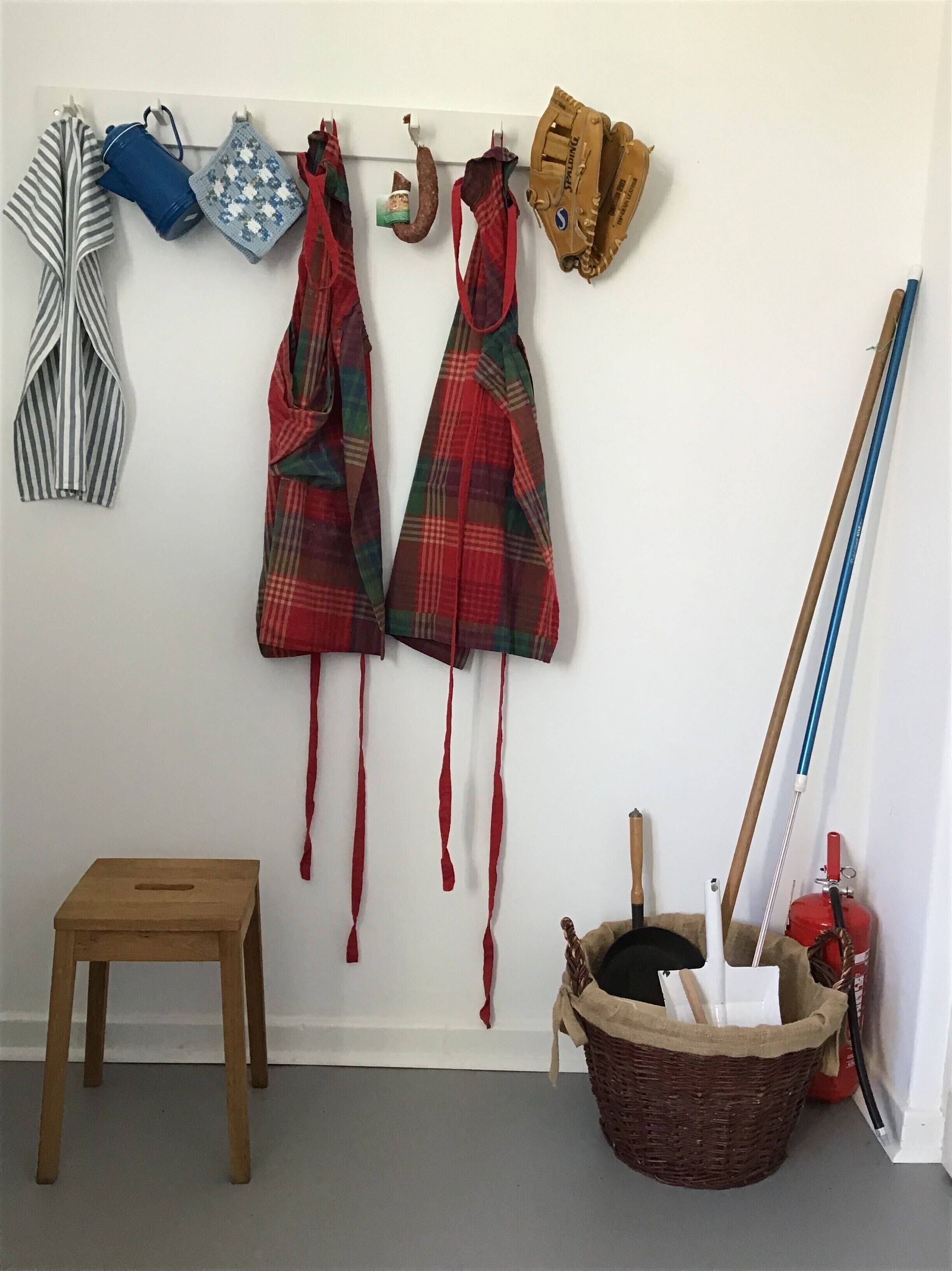 A room with a wooden stool, a basket with items, and a wall with various hanging items including a baseball glove.