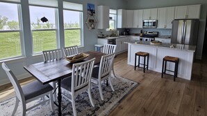 Een moderne keuken met witte kasten, een centraal eiland en een eethoek met een houten tafel en witte stoelen.