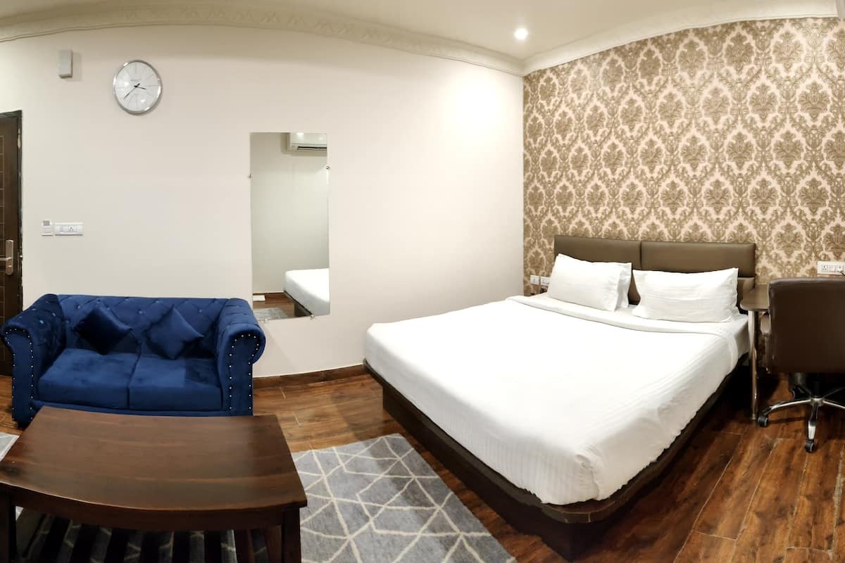 Ein Hotelzimmer mit Bett, einer Sitzecke, einem Schreibtisch, einem Fernseher und einem Spiegel.