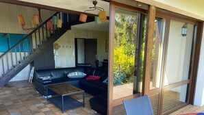 Un salon moderne avec un canapé noir, une table basse en bois et une porte vitrée donnant sur un balcon.