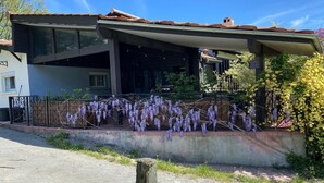 Une maison moderne dotée d’une grande baie vitrée, d’un porche en béton et de fleurs violettes.
