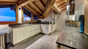A modern kitchen with white cabinets, a stainless steel sink, and a large window overlooking a snowy landscape. - Chalet 200m2 | Fireplace | Jacuzzi | Sauna | Views (Chamonix-Mont-Blanc)