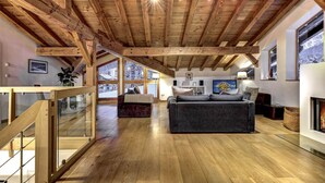 A spacious living area with wooden beams, a fireplace, and large windows offering views of the outdoors. - Chalet 200m2 | Fireplace | Jacuzzi | Sauna | Views (Chamonix-Mont-Blanc)