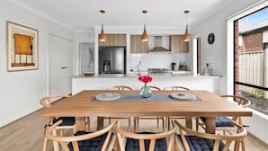 Eine moderne Küche mit Holzschränken, einer zentralen Kochinsel, Pendelleuchten und einem Essbereich mit Holztisch und Stühlen.