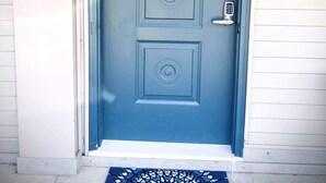 A blue door with a numerical keypad lock, a doormat with a geometric pattern, and a wall-mounted light fixture.