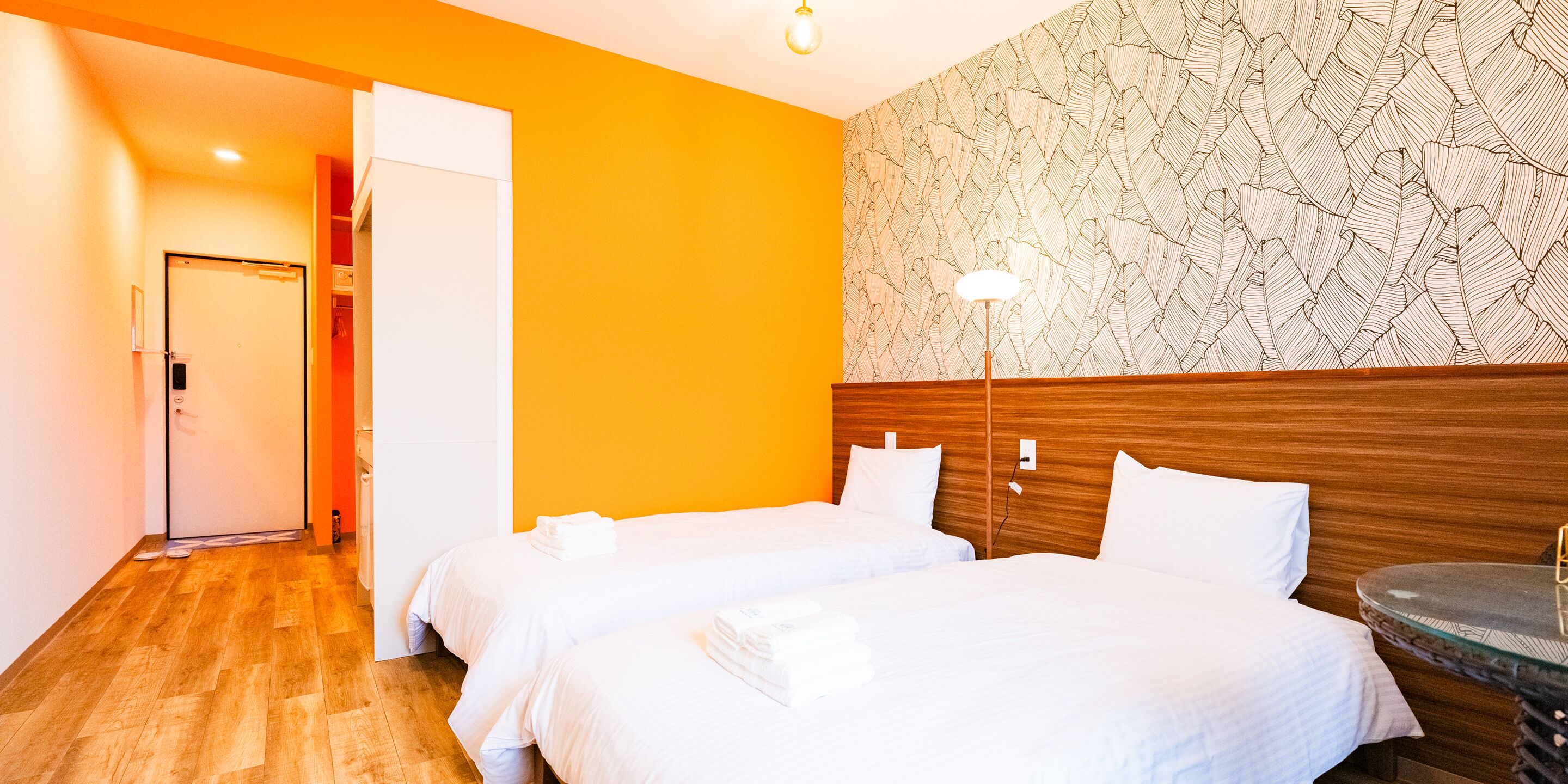 A hotel room with two beds, a wooden headboard, a patterned wall, and a small round table.