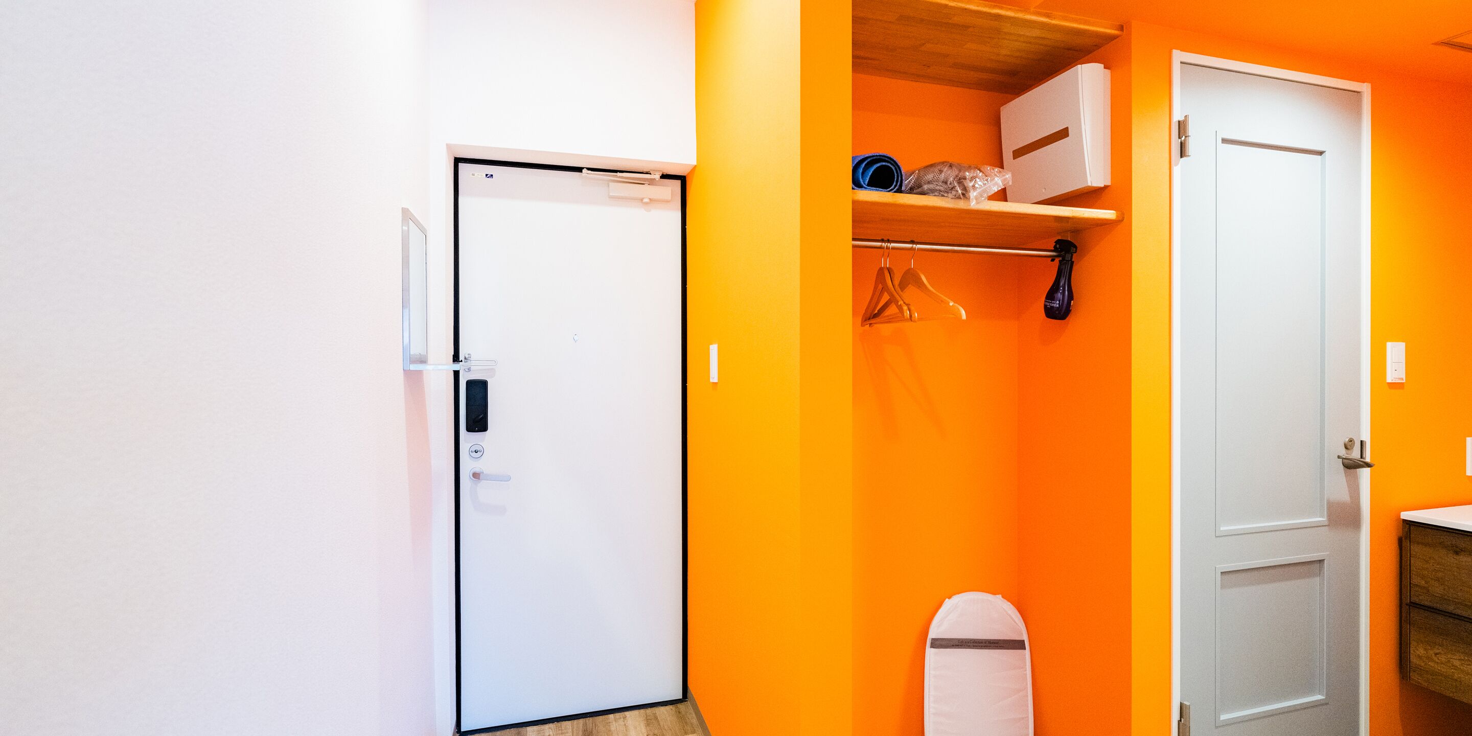 A compact room with a white door, a small shelf with items, and a wooden floor.