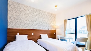 Habitación de hotel con dos camas, un papel tapiz estampado, una ventana con cortinas, una mesita pequeña y una silla.