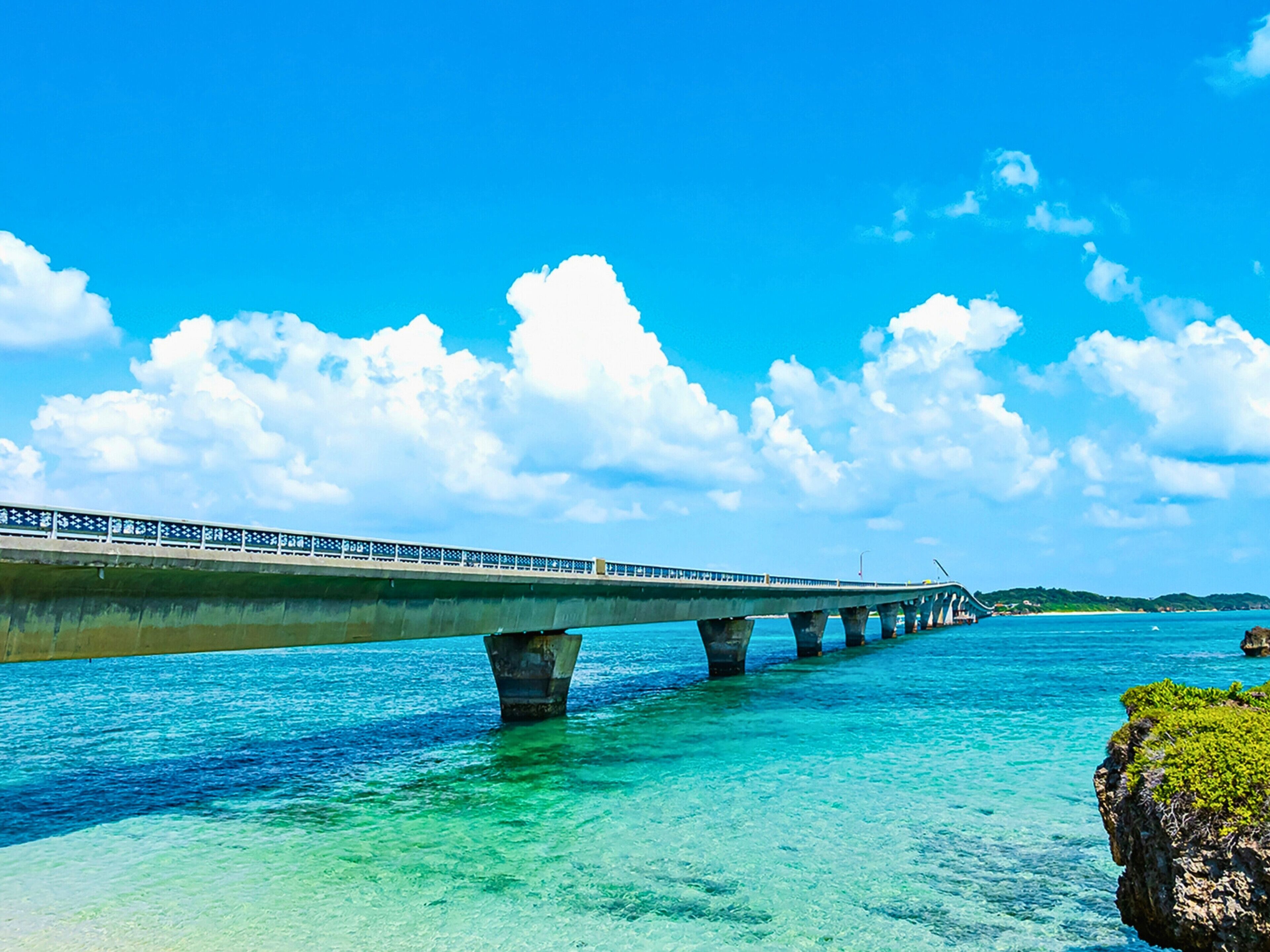 A bridge over clear blue water with a rocky outcrop on the right.