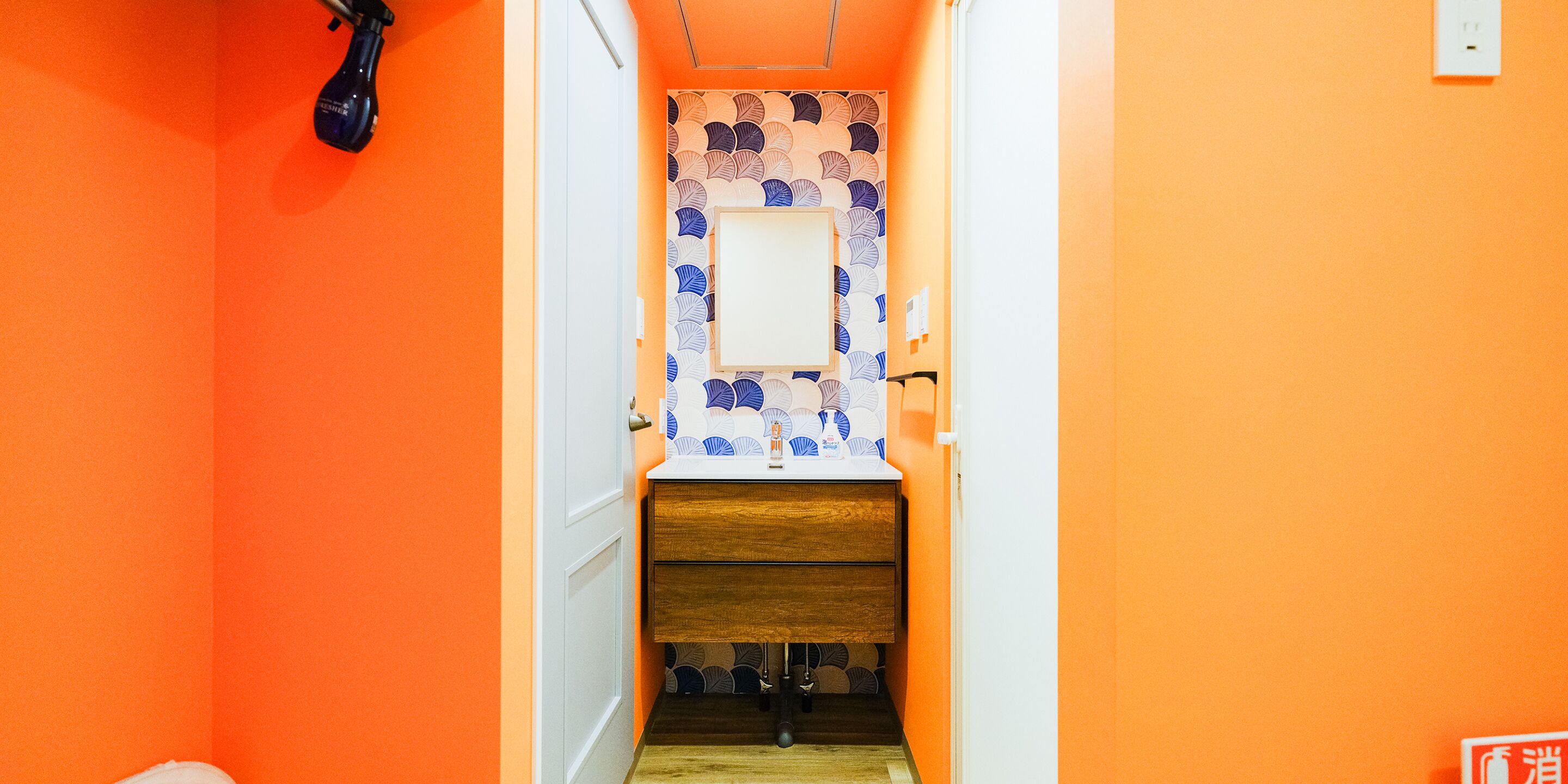 A narrow hallway with an orange wall, a white door, and a patterned wall.