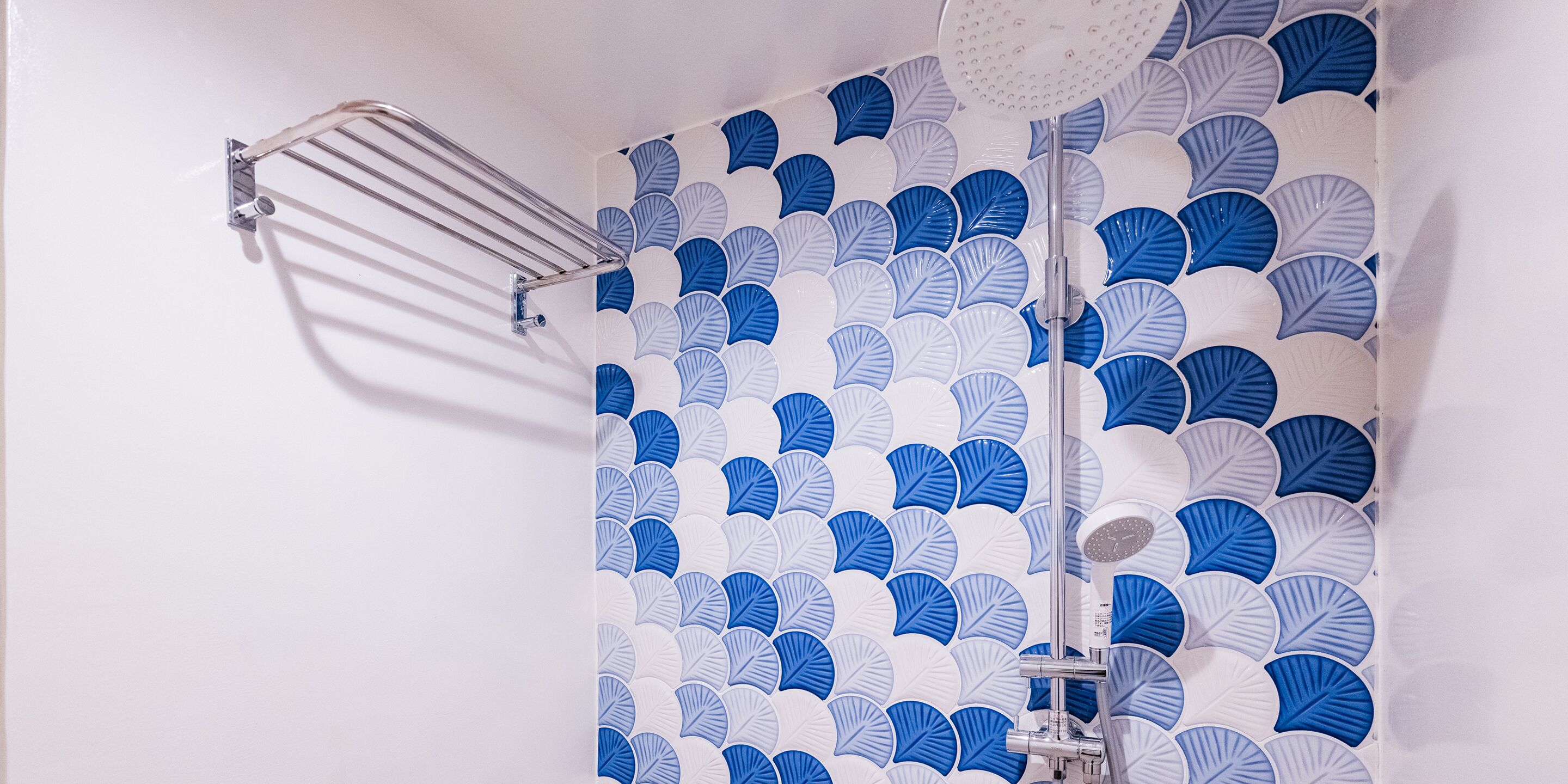 Une salle de bain avec une douche et un mur orné d’un motif de feuilles bleues et blanches.