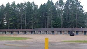 Un motel con una larga hilera de habitaciones, un área de estacionamiento y un terreno baldío al frente.