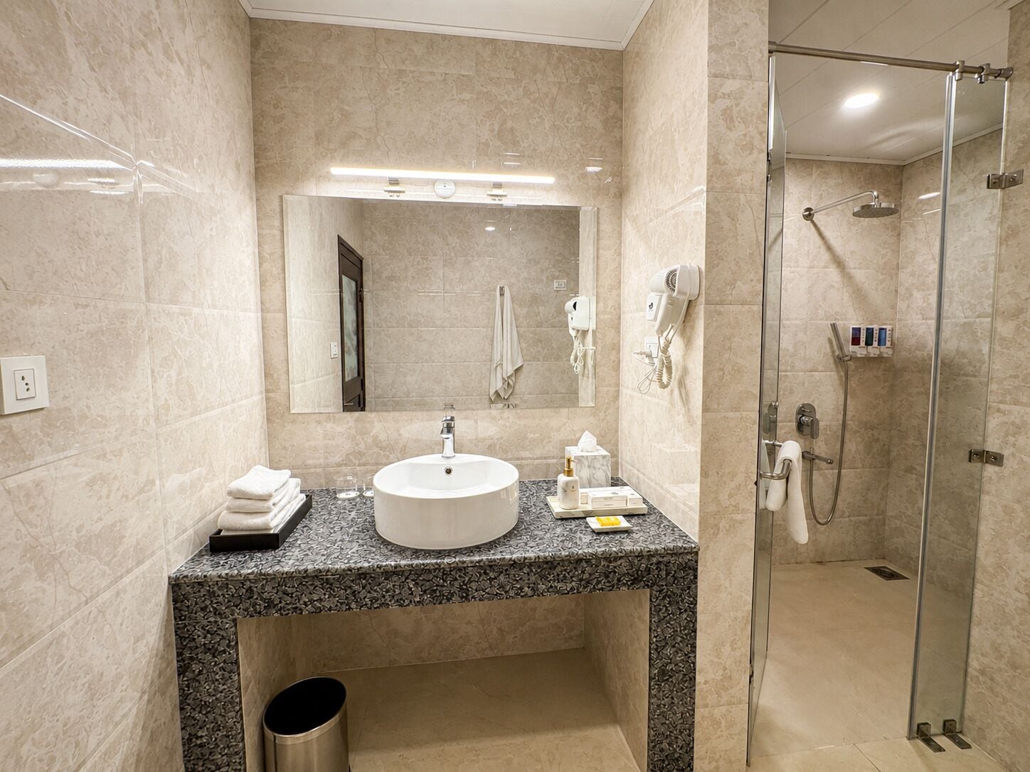 A modern bathroom with a large sink, a mirror, a glass-enclosed shower, and a marble countertop.