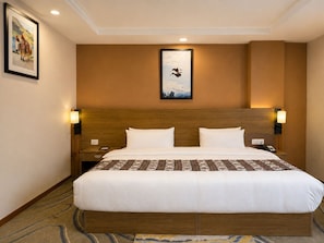 A hotel room with a large bed, two bedside tables, a nightstand, a framed picture on the wall, and a ceiling light. - Thimphu Deluxe (Thimphu)