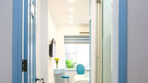 A narrow hallway with wooden flooring, a bed with a blue headboard, and a desk with a chair. - FH Homestay (Ho Chi Minh City)