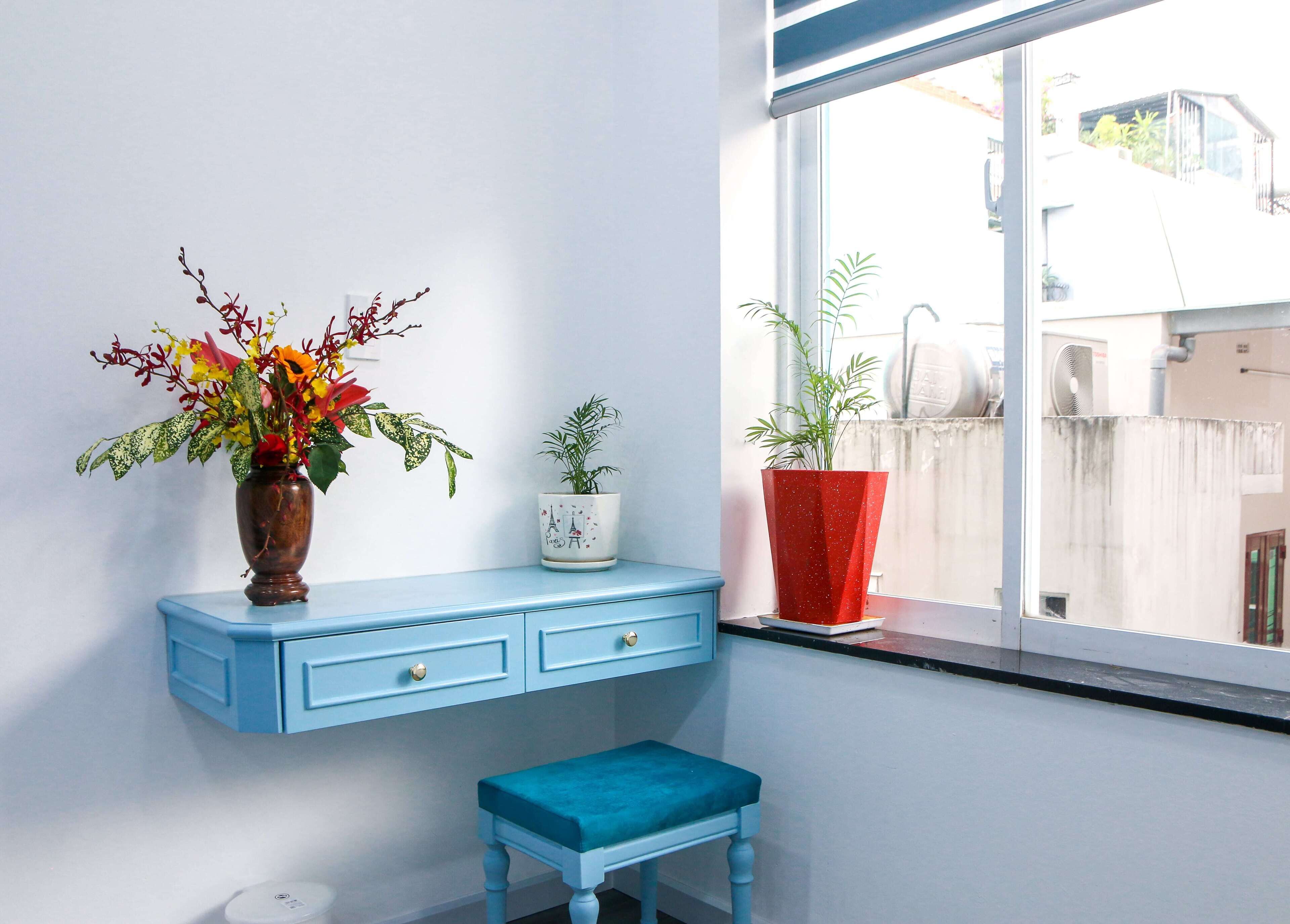 A room with a blue vanity, a small stool, and three potted plants on a windowsill.