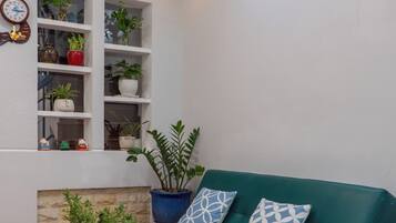 A living room with a teal sofa, a black coffee table with a white furry throw, and shelves with potted plants.