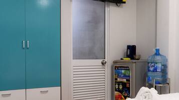 Une chambre d’hôtel équipée d’un lit, d’une armoire, d’une télévision, d’un distributeur d’eau et d’un thermostat.