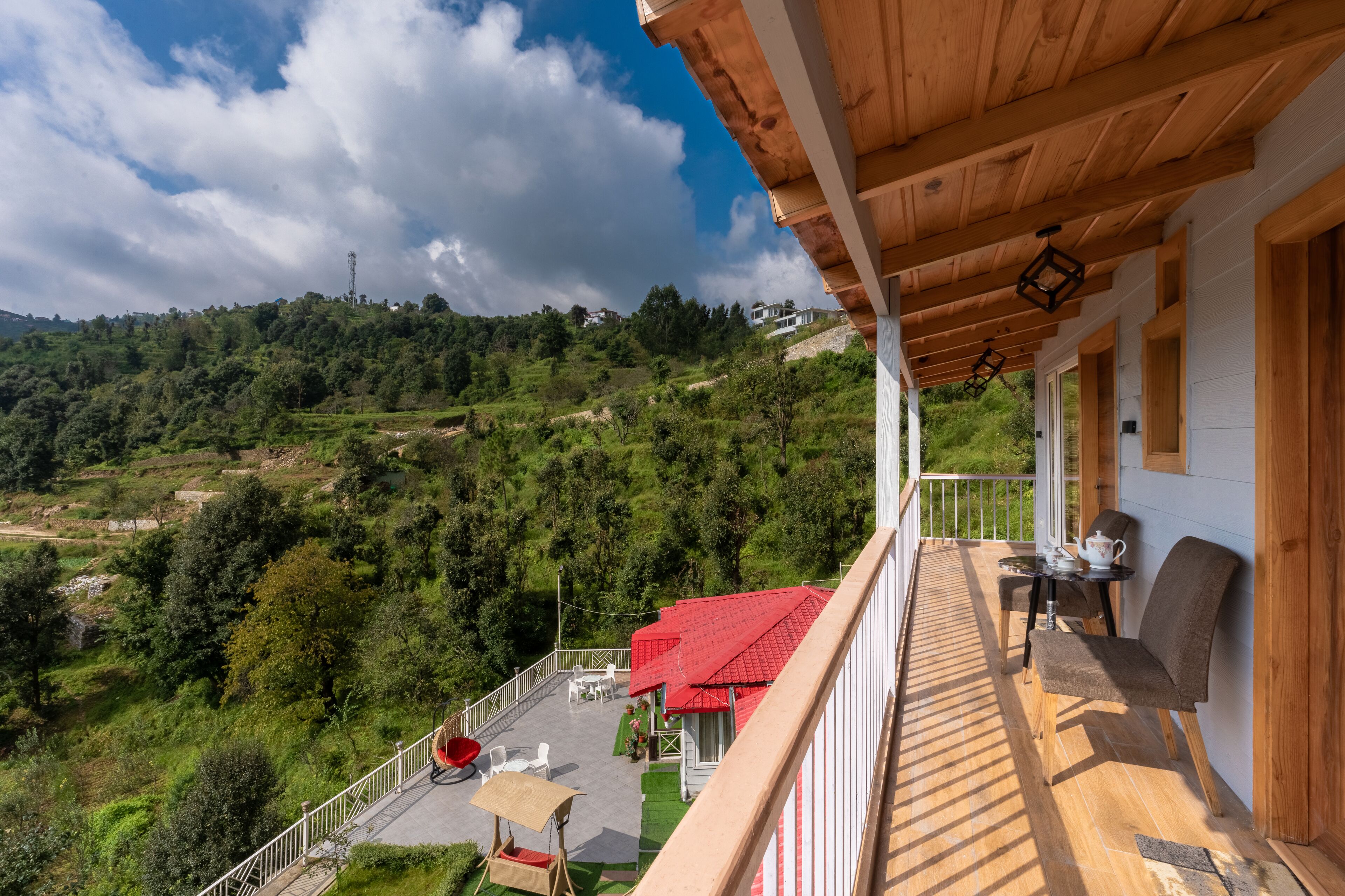 A wooden balcony with a view of a lush green landscape and a red-roofed building.